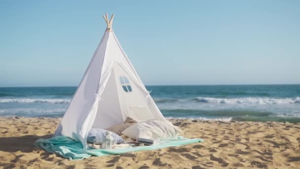 浪漫的夜晚在沙滩上 夏日的夕阳西下 沙滩上蔚蓝的天空 海浪慢速运动 浪漫的约会设置与白色帆布帐篷和蓬松的枕头在海滩上 海滨咖啡馆的概念 — 图库视频影像