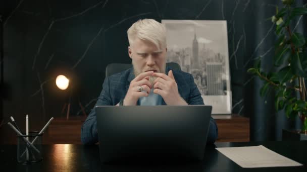 认真思考严肃的白化病青年白化病商人坐在写字台前 带着对笔记本电脑的思考 计算成本 寻找问题的解决方案 陷入沉思的概念梦想 — 图库视频影像