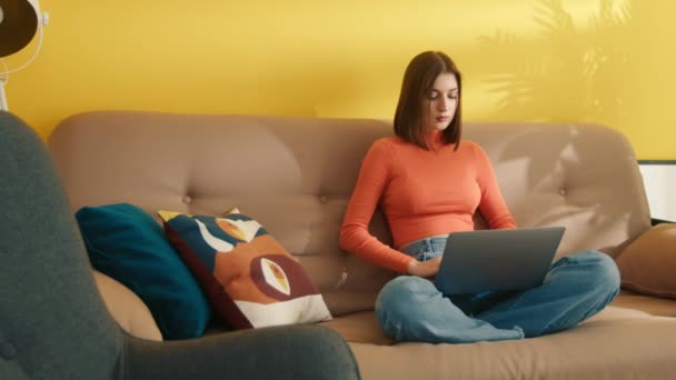 ラップトップのキーボードにタイプする忙しい女の子 自宅でオンラインで勉強するスマートな学生 試験のために準備する賢い若い女性 若い女性は宿題に集中した 快適なソファーに座っている女性モデル — ストック動画