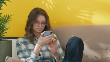 Akıllı telefon kullanan ciddi bir kadın. Cep telefonunda mesaj yazan düşünceli bir kız. Online dersler arasında dinlenen kız öğrenci. Evdeki kanepede oturan genç bayan. Gözlük takan güzel bir model.