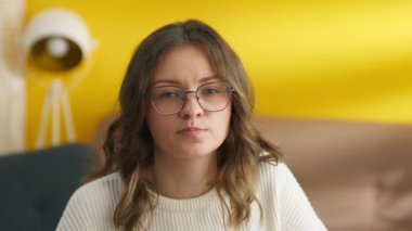 Odada kameraya poz veren akıllı kız. Üniversite öğrencisi gözlük takıyor. Gülümseyen kadın yüzü. İçerideki kameraya bakan neşeli kadının portresi. Kadın model evde eğleniyor, 4K görüntü.