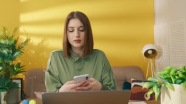Ciddi bir kadın evde dizüstü bilgisayardan öğreniyor. Akıllı telefondan mesaj okuyan odaklanmış bir kız. Cep telefonunda yazan konsantre kadın. Çevrimiçi öğrenme arasında ara veren zeki öğrenci, 4k video