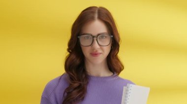 Gözlüklü neşeli kadın kamerayla flört ediyor. Sarı arka planda poz veren zeki kız. Üniversite öğrencisi not defteriyle derslere gidiyor. Dudaklarını ısıran tatlı bayan portresi. Öğrenme kavramı