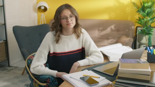 自宅で働くテーブルに座っている真面目な若い女性 カメラにポーズする眼鏡の賢い学生の肖像画 ラップトップのオンラインレッスン後に休憩する自信のある女性 教育コンセプト — ストック動画