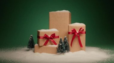 Kar yığınları altın hediye kutularının üzerinde zarif saten kırmızı fiyonklar ve yeşil arka planda izole çam ağaçları figürleri. Kış harikalar diyarı konsepti sunar. Noel arifesi için sürpriz hediyeler Mutlu 2024
