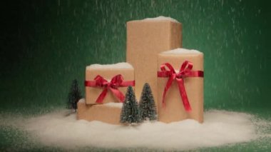 Işıltılı altın hediye kutularına yağan yoğun kar, zarif saten kırmızı fiyonklar ve yeşil arka planda izole çam ağaçları figürleri. Noel için sürpriz hediyeler. Mutlu 2024 Yeni Yıl sunumları