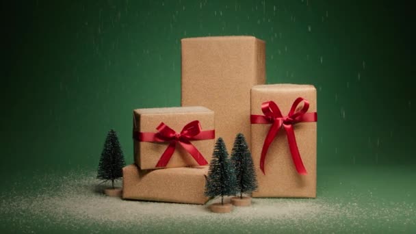 エレガントなサテン赤い弓と松の木が緑の背景に隔離されたゴールデンギフトボックスの積み重ねに落ちる雪 クリスマスのサプライズプレゼント ハッピー2024 新年のプレゼントバックグラウンド4K — ストック動画
