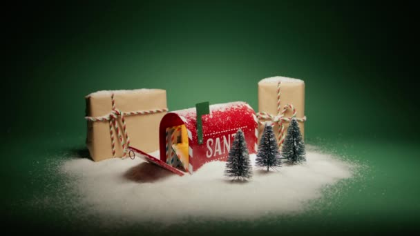雪の下に贈り物とクリスマスの装飾とオープンレッドメールボックスでサンタへの手紙 ドリーは緑色の背景にあるギフトボックスの赤いカメラを撮影した ウィンターワンダーランド 希望のクリスマスの背景コンセプトを作る — ストック動画