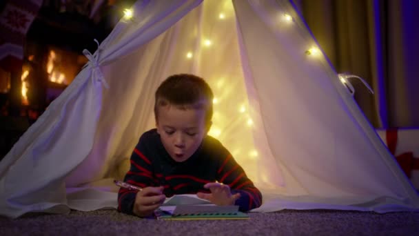 Söt Pojke Skriver Ett Brev Till Jultomten Med Önskningar Liggande — Stockvideo