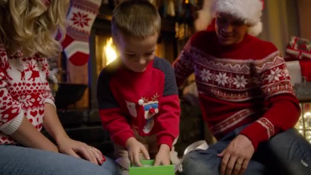かわいいキッズラッピングギフトボックス 装飾されたクリスマスツリーの近くにサプライズプレゼントを得ることに興奮する超幸せな小さな少年 暖炉に座っている幸せな家族 シネマティッククリスマスイブレッドカメラ — ストック動画