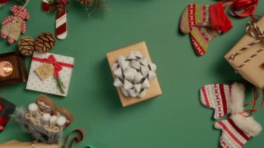 Mutlu Noeller Kırmızı Kamera 4K. Yeşil zemin üzerinde parlak gümüş bir fiyonk olan zarif el işi kağıt hediye kutusunun yukarıdan görünüşü. Web sitesi ve sosyal medya kampanyaları için harika bir tatil reklamı.