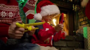 Küçük baba ve küçük çocuk şirin Noel Baba şapkalı çocuk şöminede renkli uçaklarla komik bir oyun oynuyorlar. Mutlu erkek aile babası ve küçük çocuk Noel arifesinde oyuncak uçakla eğleniyorlar.