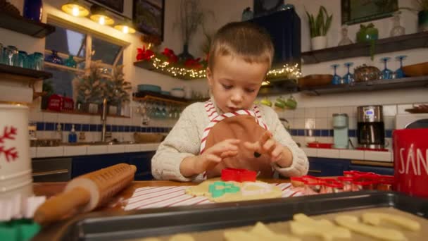 クリスマスクッキーカッターを使用してジンジャーブレッドクッキーを作るかわいい男の子は お祝いの形に生地をカットするために 遅い動きRedカメラ4K クリスマス休暇中にキッチンで料理するハッピーキッド — ストック動画