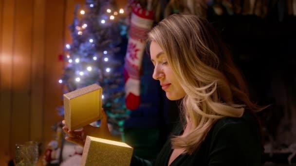 圣诞前夕 在装饰过的圣诞树旁 快乐而惊讶的女人收到了心爱的男人送给她的圣诞礼物 美丽的女性在假日从心爱的情人那里打开礼物 冬季庆祝4K — 图库视频影像