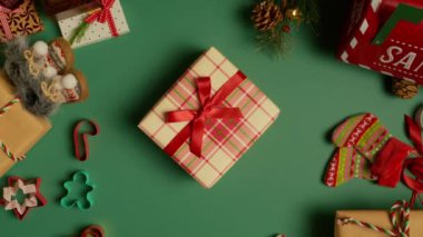 Yeşil arka plan ve Noel süslemeleri üzerine ekose kağıdında saten kırmızı kurdeleyle bağlanmış hediye kutusu, kırmızı Noel Baba posta kutusu, düz yatar vaziyette dönen kurabiyeler, 4K kamera görüntüsü
