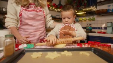 Genç anne, küçük çocuğa fırından önce hamur bisküvilerini pişirme tepsisine koymayı öğretiyor. Noel zamanı, aile eğlencesi. Geleneksel Noel kurabiyeleri pişirme süreci