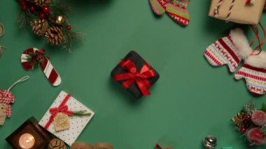 Dönen çam yeşili arka planda parlak kırmızı saten kurdeleli zarif kadife hediye kutusu. En tepeden aşağıya prestij siyah hediye kutusu ve Noel dekoru 4K ile çevrili kurdele.