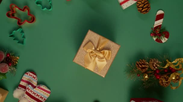 パイングリーンの背景を回転させるショットの真ん中に置かれた光沢のあるゴールデンギフトボックス クリスマスの装飾4Kのリボンが付いている上下の眺めの威信の黄金の現在の箱 — ストック動画
