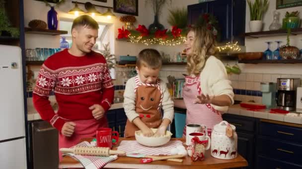 年轻快乐的家庭带着孩子跳舞开心的笑着在家里准备圣诞晚餐 寒假期间和儿子一起愉快地做饭的快乐夫妻 红色相机 — 图库视频影像