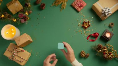 Adam nişan yüzüğüyle birlikte güzel bir hediye kutusu tutuyor ve kapağını açıyor. Yeşil Noel arka planında açık mavi mücevher kutusu açılıyor. Hediye ya da sürpriz kavramı, yukarıdan aşağı görünüm, yavaş çekim 4K öneri