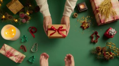 Yavaş çekim hediye videosu. Üst görüşlü adam kırmızı ipek kurdeleli altın kutuyu sürpriz hediyeli kadına veriyor. Yeşil Noel arkaplanından hediye. Kış tatili, Mutlu Noeller.