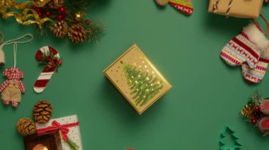 Yeşil arka planda çekimin ortasına yerleştirilmiş, üzerinde parlak altın yıldızlar olan zarif hediye kutusu. En tepeden aşağıya, prestijli hediye kutusu Noel süsleriyle çevrili 4K