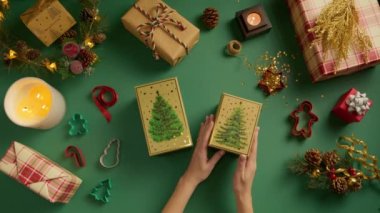 Yeşil altın hediye kutusunu açan kadınların elleri, Noel ağacı ve Noel ve yeni yıl süslemeleriyle dolu yeşil arka plana çam ağacı çiziyor. Üst görünüm düz, kırmızı kamera 4K 'da yatıyordu.