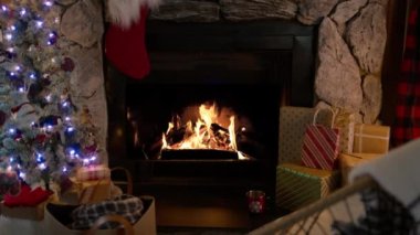 Evde sıcacık şömine, sinematik Noel dekorasyonlu kamera görüntüleri. Noel ağacının hafif çelengi ve ağır çekimde yanan sıcak altın alevleriyle kapalı bir ortamda kış mevsimi.
