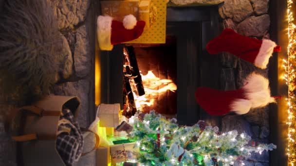 プラスチック偽のクリスマスツリーが付いている垂直方向の映像は燃える森が付いている暖炉の近くの輝く軽いガーランドそしてギフトを飾りました Redカメラのシネマティックショット Xmasバックグラウンドモバイルコンテンツ4K — ストック動画