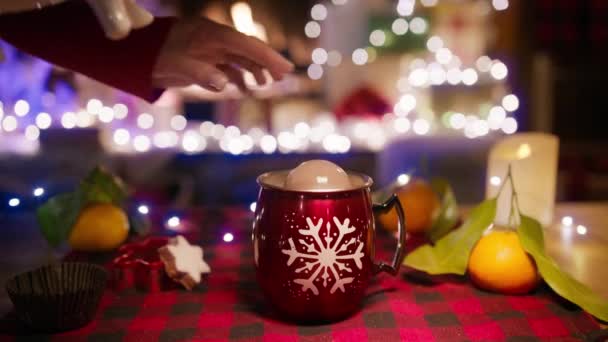 女性の手はチョコレート爆弾を熱いココアに置き 暖炉で平らなナプキンに雪のフレークと赤いコップの形でクリーマーピッチャーからトップホットミルクをこぼします クリスマス 冬休み — ストック動画