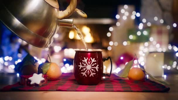 赤いスノーフレークマグで金属のケトルから熱湯を注ぐ クリスマスガーランドと部屋で美味しいホットチョコレートドリンクを作るためにホリデーカップに蒸し水をこぼし 冬に暖炉を燃やします — ストック動画