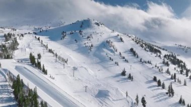 Güneşli kış gününde, kalın buz gibi kar tabakasıyla kaplı dik dağ tepelerinden inen kayakçılarla kayak pisti. Mammoth Lakes kayak merkezinin kayak koltukları, Kaliforniya Havacılık Kurumu