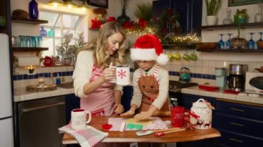 Geniş kırmızı Noel Baba şapkalı, sevimli, anaokulu çocuğu olan genç sarışın bir kadın Noel arifesinde tatlı pastalar pişiriyor, sohbet ediyor, şenlikli ev mutfağında aşçılığın tadını çıkarıyor. Tatiller 4K yaşam tarzını kutluyor