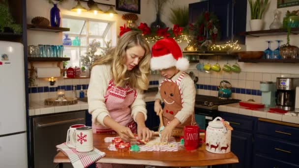 豪華なサンタハットの小さなヘルパーの息子は かわいいプリスクーラーと若いブロンドの母親と一緒にクリスマスイブクッキーを調理し お祝いの装飾された家庭のキッチンで料理を楽しんでください 休日のお祝い — ストック動画
