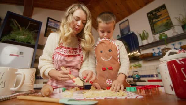 穿着圣诞围裙的年轻漂亮女人和儿子一起在厨房做饭 可爱的孩子穿着姜饼围裙准备圣诞饼干 把剪裁后的形状和花生酱一起享用过程 — 图库视频影像