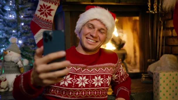 Przystojny Uśmiechnięty Mężczyzna Czerwonym Swetrze Zimowym Santa Kapelusz Pomocą Smartfona — Wideo stockowe
