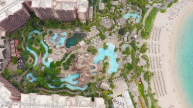Mükemmel kumlu sahil havası Oahu. Lüks otel manzarası, eğlenceli su parkı ve manzaralı yeşil bahçe, çocuklar ve aileler temiz mavi suda yüzüyor. Hawaii adasında yaz tatili 4K