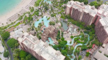 Lüks otel manzarası, eğlenceli su parkı ve manzaralı yeşil bahçe, çocuklar ve aileler temiz mavi suda yüzüyor. Hawaii Adası 4K 'da yaz tatili. Mükemmel kumlu sahil havası Oahu