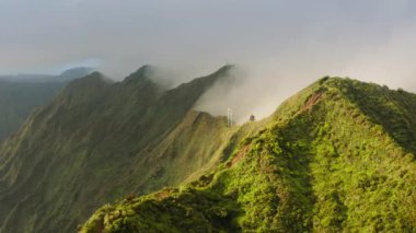 Cennete giden merdiven, Oahu adasındaki Haiku Merdivenleri 'nin tepesinden manzara. Dik tepe ve dikey eğim 4K ile destansı yeşil dağ zirveleri. Güneşli gündoğumunda dramatik Hawaii bulutlu havası