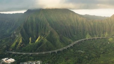 Hawaii 'deki Oahu Adası' ndaki sinematik dağlar arasındaki dolambaçlı dağ yolunun üzerinde çekilmiş hava görüntüleri. Altın güneşli bulutlu yaz gündoğumu. H3 otoyol tünelleri ABD turizmi tarafından sürülen arabalar
