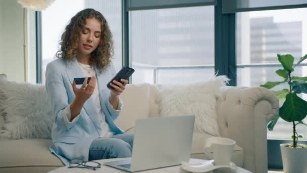 即座に簡単なモバイル決済を使用して幸せな女性の買い物客 オンラインストアで購入する顧客 Eバンキングアプリ スマートフォンとクレジットカードを持っている笑顔スタイリッシュな女性がソファーに座って現代の家 — ストック動画