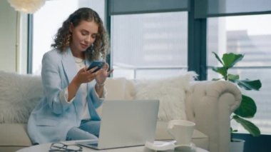 Evde akıllı telefon kullanan gülümseyen genç bir kadın. Cep telefonu tutan olumlu bir milenyum kızı. Sosyal medyaya abone olan çekici blogcu, internetten ürün sipariş eden veya 4K uygulamasında internetten satın alan