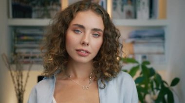 Modern apartman arka planında kameraya bakan genç, lüks ve seksi bir kadının portresi. Doğal makyajlı profesyonel modelle yüzleş açık mavi gözlü bayan 4K RED kamera