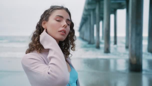 在阴郁的夏日 身穿亮晶晶蓝色丝滑裙和米黄色休闲羊毛衫的慢镜头女主角 走在海滨的海滨码头上 度假的女游客 — 图库视频影像