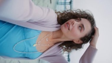 Güzel kadın dikey portresi. Selfie videosu için poz veren muhteşem Avrupalı manken. Gülümseyen nüfuzlu blogcu yüze dokunuyor ve doğal kıvırcık saçlı. Moda ve güzellik konsepti plaj geçmişi