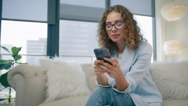 聪明的年轻女人穿着时髦的眼镜用智能手机 迷人的自由职业者企业家发短信给合作伙伴 在互联网应用程序4K Red上管理项目 拿着手机的千禧女孩 — 图库视频影像