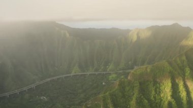 İnsansız hava aracı destansı manzaranın üzerinde bulutlar içinde uçuyor ve etkileyici bir yol yapımı olan Hawaii havası var. Nefes kesici Oahu doğa manzarası sinematik altın gün doğumunda bulutlar yüksek yeşil zirvede asılı