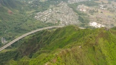 Hawaii adasında Cennet 'e giden destansı merdivenlerin hava manzarası. Yeşil dağın altındaki manzaralı otoyol. Eski radyo donanma uydu inşaatı üzerinde uçan insansız hava aracı, İkinci Dünya Savaşı 'ndan kalma endüstriyel askeri bina.