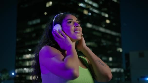 在市中心听音乐的年轻而清凉的混血儿嬉皮士 在户外享受夜晚的城市4K 穿着耳机独自在夜市大街上跳舞的性感的非洲裔美国女人 — 图库视频影像