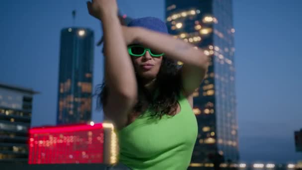 穿着霓虹灯绿色上衣 头戴紫色斗篷帽的活跃的非洲裔美国黑人妇女在市区的夜色背景下跳舞 才华横溢的混合型女舞蹈家有节奏地跳4K慢步舞 — 图库视频影像